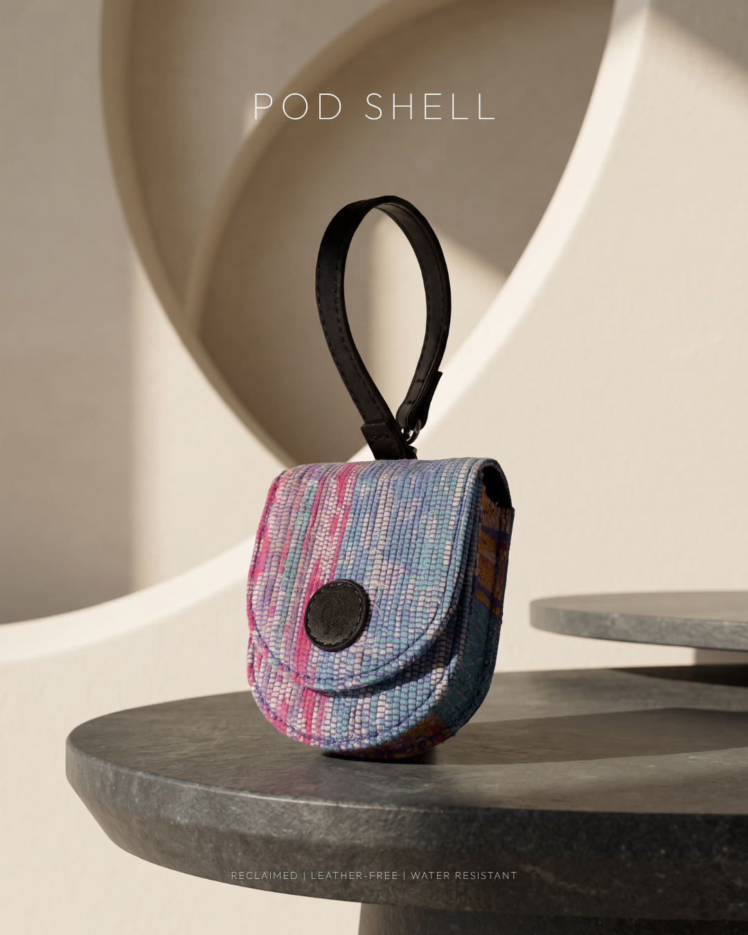 Small reclaimed fabric (khesh) pouch showing the woven multicolour panel and wrist loop, on a dark stone pedestal
