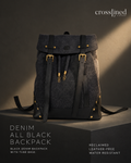 A Cross Lined backpack in dark denim and black tyre tube, displayed on a dark pedestal with dramatic side lighting. The backpack features a flap top with brass-tone buckles, drawstring details, and gold-tone rivets.