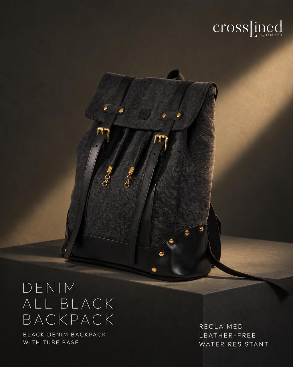 A black denim backpack with tyre tube straps and gold-tone hardware, displayed on a dark pedestal in a studio setting with dramatic lighting. The brand name 'crosslined' is visible in the top right corner.