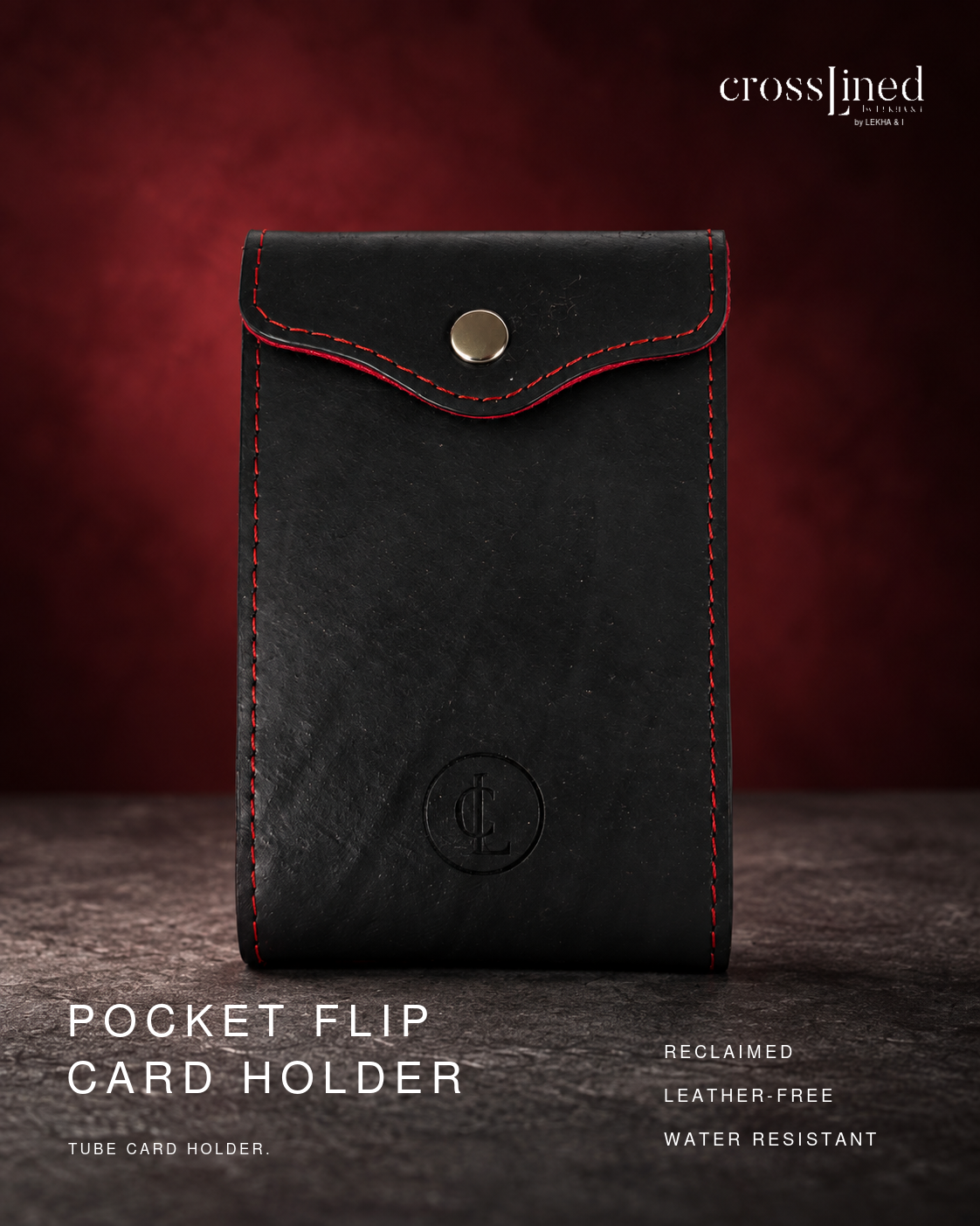 A black leather-free tube card holder with red contrast stitching and a gold snap button, shown upright on a dark wooden surface against a deep red background. Text on the image reads 'crosslined by christine' and 'POCKET FLIP CARD HOLDER'.