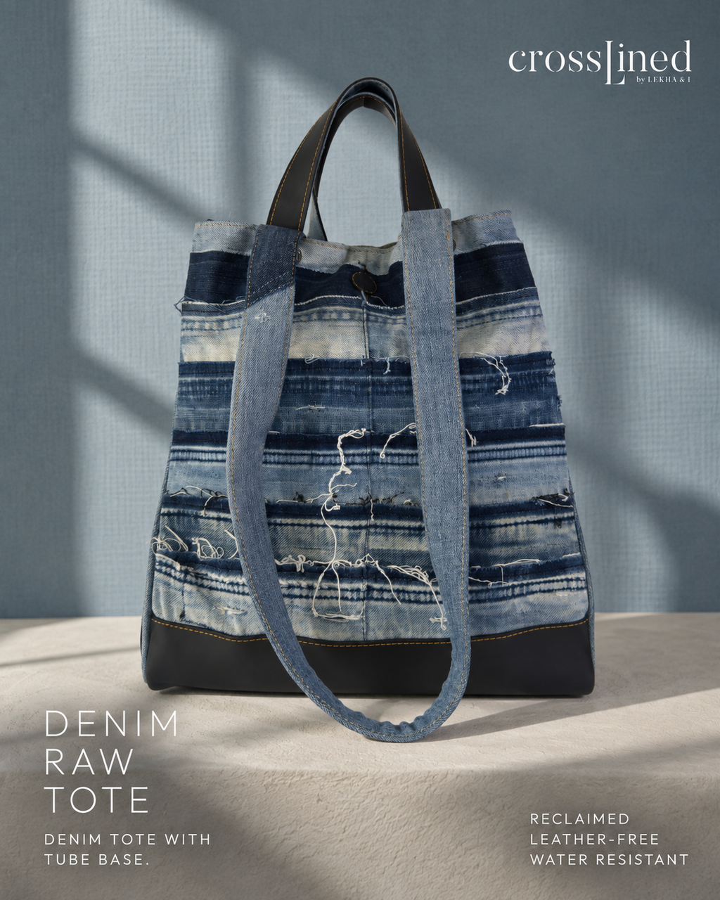 A Crosslined denim tote bag made from reclaimed blue denim strips, featuring a black tyre tube base and handles, set against a textured blue-gray background with soft shadows.