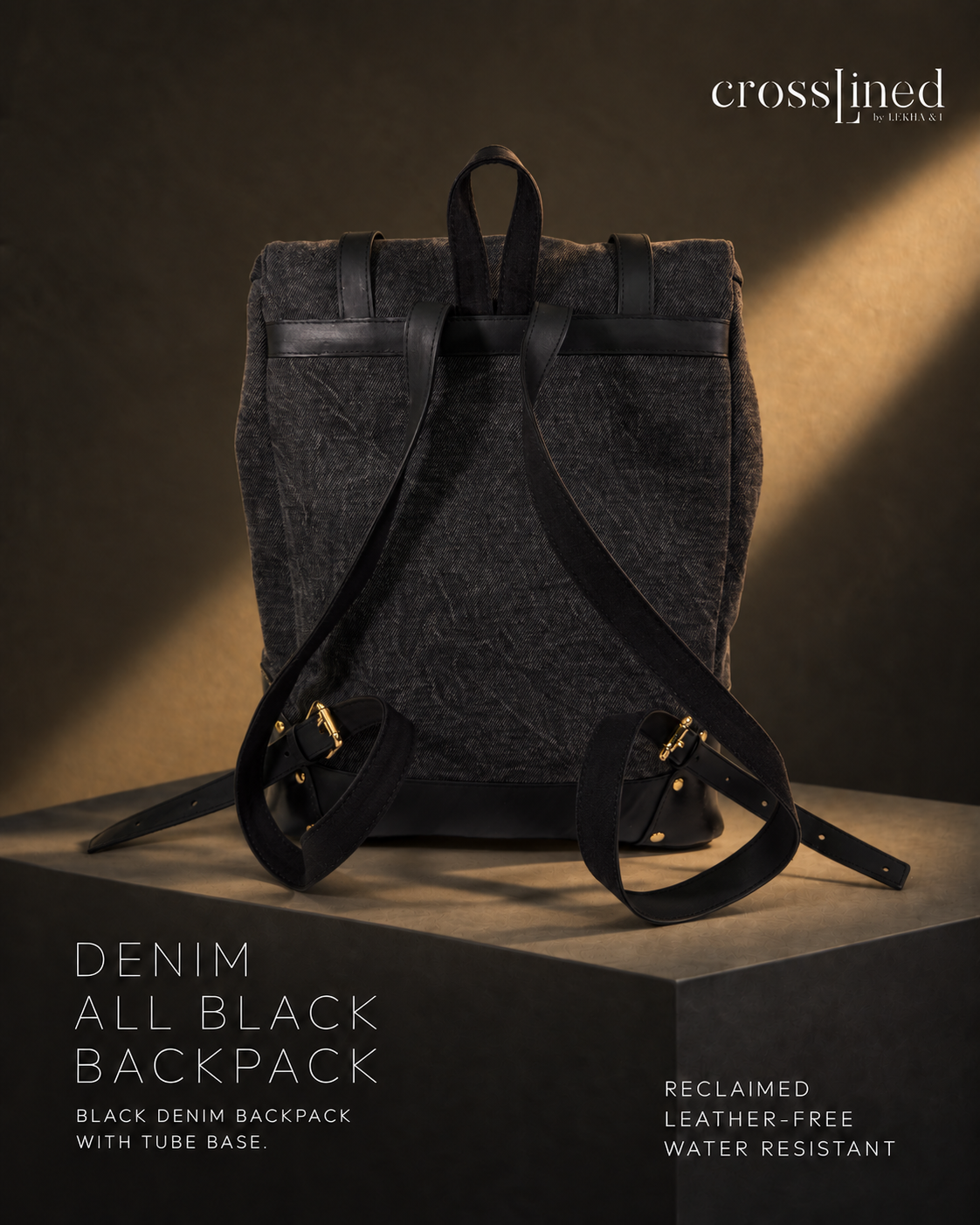 A black denim backpack with black tyre tube straps and gold-tone hardware, displayed upright on a dark pedestal against a warm brown studio background. Text on the image reads 'crosslined' and 'DENIM ALL BLACK BACKPACK'.
