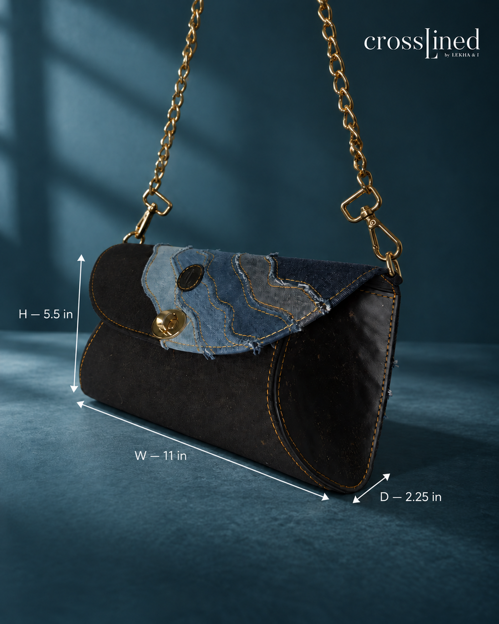A black tyre tube body denim clutch bag with a gold chain strap, shown with dimension lines indicating height, width, and depth. The background is a dark blue textured surface with soft shadows, and the 'crosslined by lekha & i' brand logo is visible in the top right