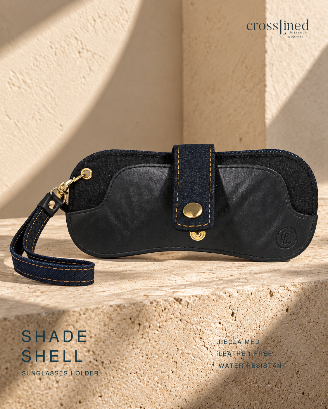 A black sunglasses holder case with a wrist strap and gold-tone hardware, photographed on a textured beige stone surface in warm sunlight. The brand name crossjined appears at the top right, and text at the bottom reads 'SHADE SHELL SUNGLASSES HOLDER'.